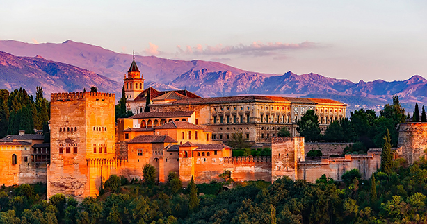 Colorful sunset view of the ancient Alhambra palace with mountains in the background.
