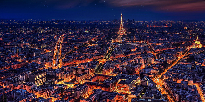 Nighttime aerial view of Paris with the streets and Eiffel Tower lit up.