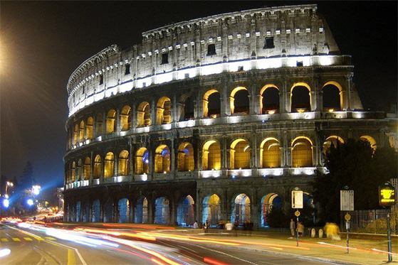 Nighttime time lapse view of 4 levels of arches on the Coloseum with the blur of lights from cars on the street driving by.